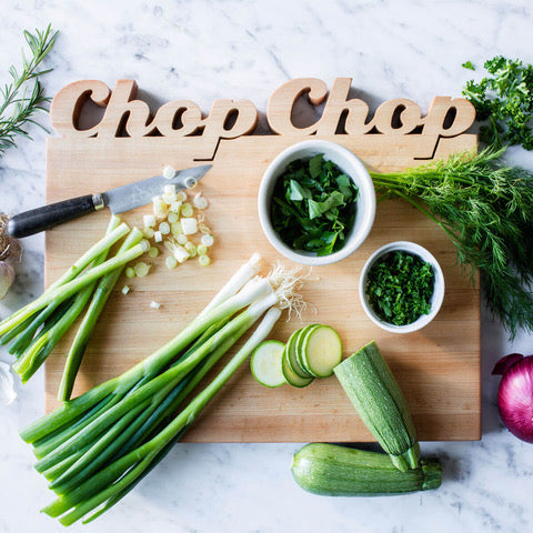 Maple Personalized Cutting Board with Words Chop Chop cut out on top. The board has a knife, green onions, parsley, and a cucumber on top.