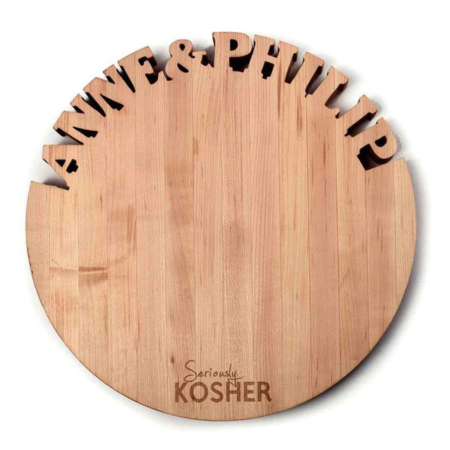The Names Annie & Phillip carved out on the top of a light wood round cutting board with Kosher on the bottom for Jewish family kitchen gift.